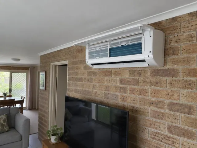 Clean split system with open front panel and visible filters on a brick wall in a living room in Pacific Pines