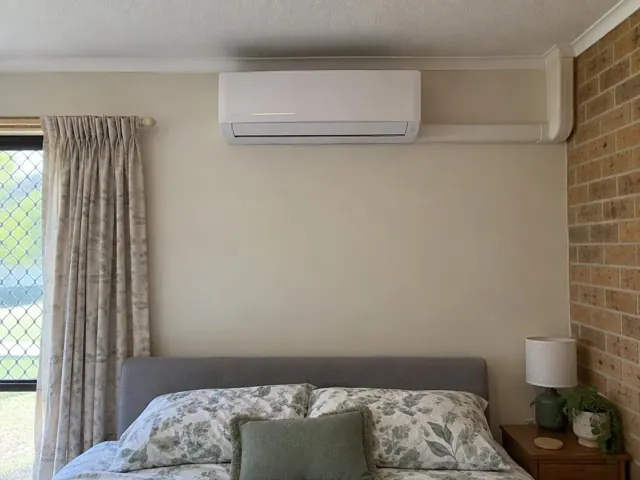 Wall-mounted split system above a bed in a carpeted bedroom with brick feature wall in Coomera